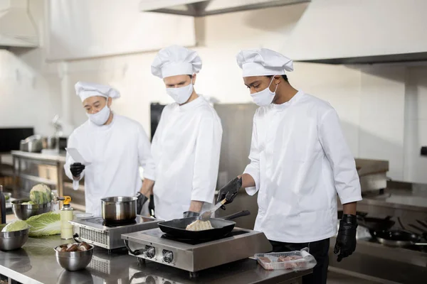 다양 한 인종으로 구성된 요리사들 이 유니폼을 입고 주방에 있는 식당을 위해 마스크를 쓰고 식사를 한다 — 스톡 사진