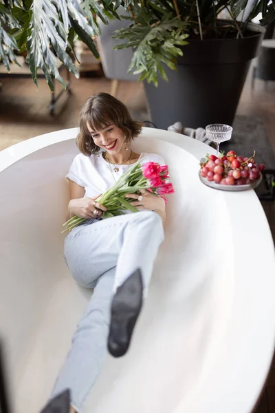 女人躺在浴缸里，手里拿着一束郁金香 — 图库照片