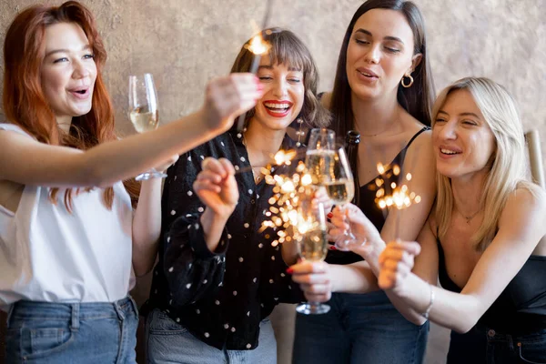 Kız arkadaşlar köpüklü şarap içip havai fişekleri ateşliyor, evde kutluyorlar. — Stok fotoğraf