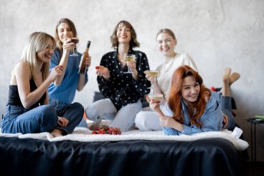 Yetişkin kız arkadaşlar eğleniyor, evde yatakta birlikte oturuyorlar.