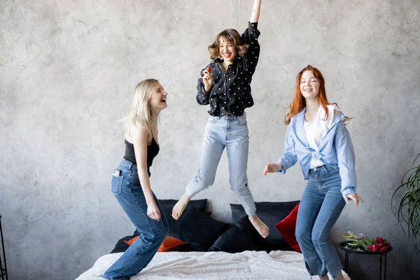 Yetişkin kız arkadaşlar eğleniyor, yatakta birlikte zıplıyorlar. — Stok fotoğraf