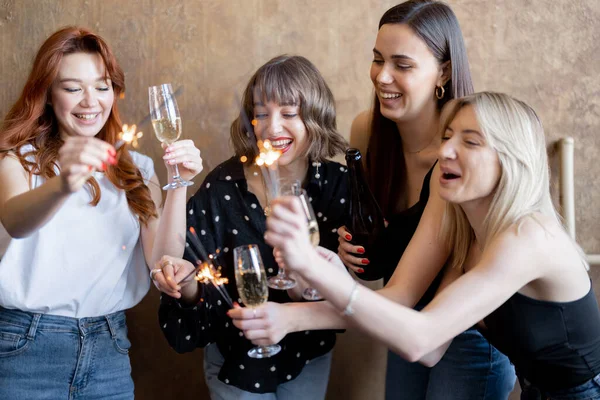 Kız arkadaşlar köpüklü şarap içip havai fişekleri ateşliyor, evde kutluyorlar. — Stok fotoğraf