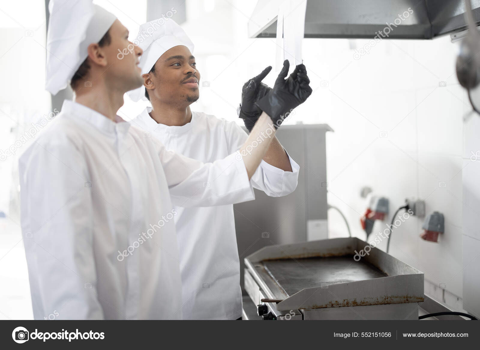 Chefs look on printed checks with orders while cooking in the