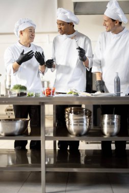 Farklı milletlerden aşçılar restoran menüsü için pişirilmiş yemekleri tadıyorlar.