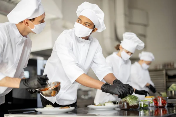 Grupo de cocineros terminando platos principales mientras trabajan juntos en la cocina —  Fotos de Stock