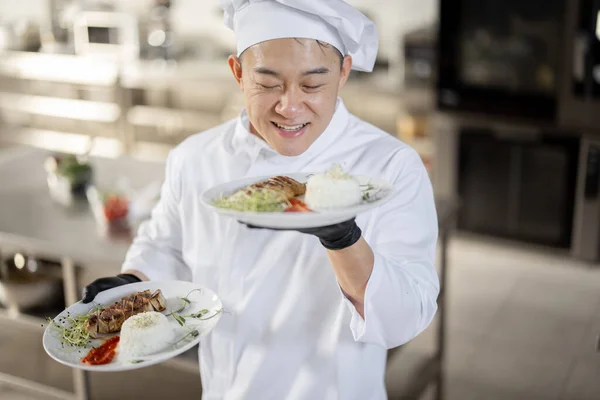 Portret van lachende chef-kok in uniform staand met kant-en-klaar maaltijd in de keuken — Stockfoto