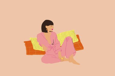 Mavi pijamalı esmer kadın bej arka planda rahatça oturuyor.