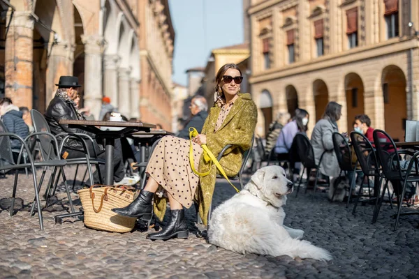 Mujer sentada con su perro blanco en la cafetería al aire libre en el casco antiguo de la ciudad de Bolonia —  Fotos de Stock
