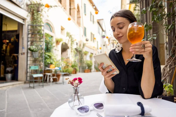 Donna che usa il telefono mentre si siede con il vino al ristorante italiano su strada accogliente — Foto Stock