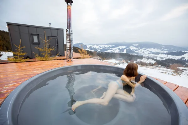 Mujer nada en baño caliente mientras descansa en una pequeña casa moderna en las montañas — Foto de Stock