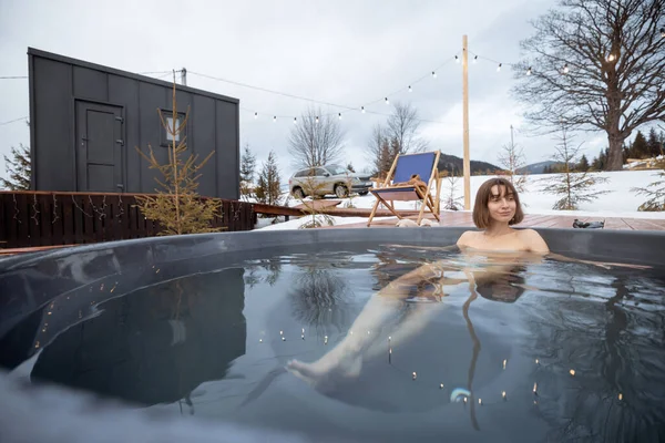 Mujer nada en baño caliente mientras descansa en una pequeña casa moderna en las montañas — Foto de Stock