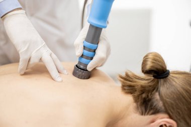Doktor erkeklerin omzuna şok dalgası tedavisi uyguluyor.
