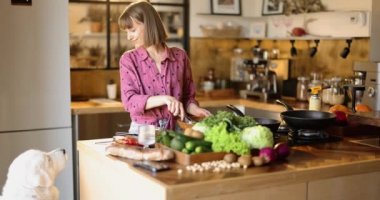 Sağlıklı yemek pişiren ve köpeğini mutfakta besleyen bir kadın.