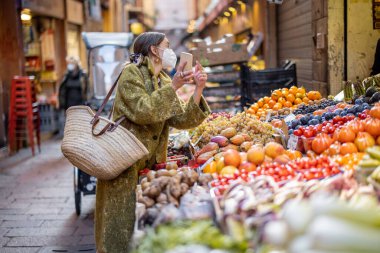 Kadın salgın sırasında sokak pazarından yiyecek alıyor.