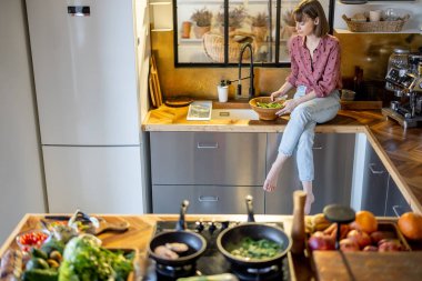 Modern mutfakta salata yiyen bir kadın.