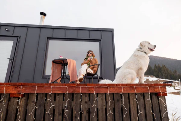 Köpeğiyle birlikte doğadaki küçük evin terasında dinlenen bir kadın. — Stok fotoğraf