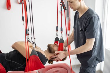 Rehabilitasyon uzmanı erkek hastaya süspansiyon kayışları üzerinde aktif tedavi uyguluyor.
