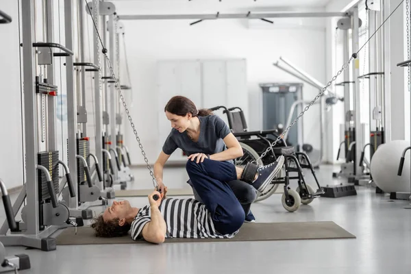 Rehabilitation specialist helps a guy to do exercise on decompression simulator for recovery — Stock Photo, Image