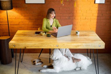 Kadın rahat evdeki ahşap masada otururken dizüstü bilgisayarla çalışıyor.