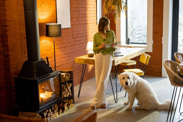 Kadın rahat oturma odasında köpeğiyle dikilirken dijital tabletle çalışıyor. — Stok fotoğraf