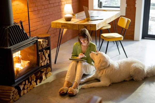 Femme travaille sur tablette numérique avec un chien près de la cheminée — Photo
