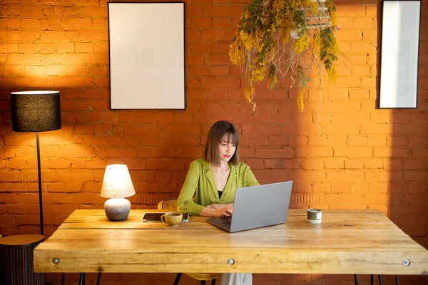 Woman works on laptop while sitting by the wooden table at cozy home — Stock Photo, Image