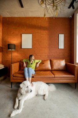 Kanepede dinlenen ve evde beyaz köpeğiyle oynayan bir kadın.