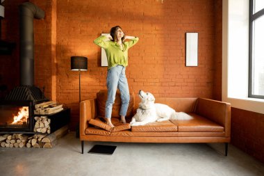 Evdeki kanepede köpeğiyle eğlenen bir kadın.