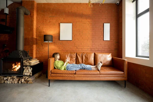 Woman using phone while relaxing on a leather couch at home