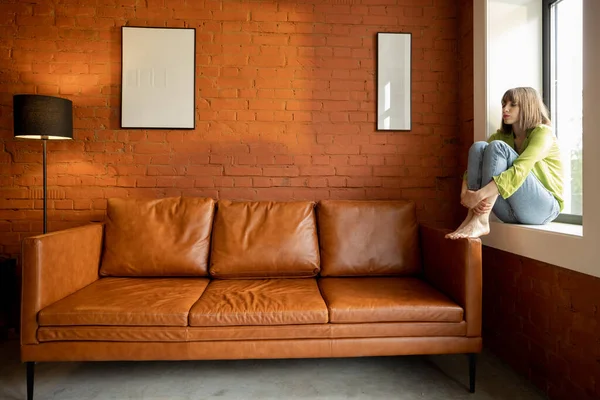 Kadın pencerenin pervazında tek başına oturuyor.