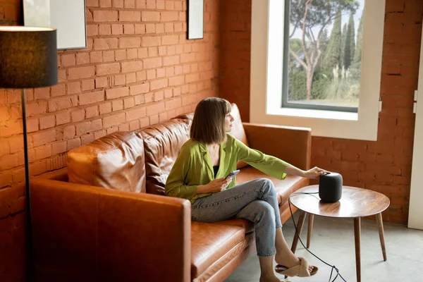 Mujer tocando altavoz inteligente mientras está sentado en el sofá en casa — Foto de Stock