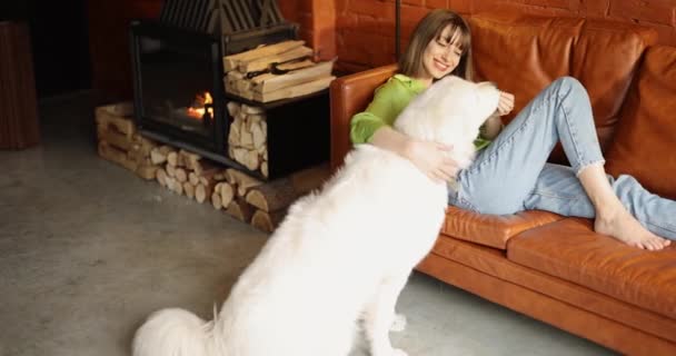 Ung kvinna som använder telefon medan du sitter avslappnad med sin söta vita hund på en soffa — Stockvideo