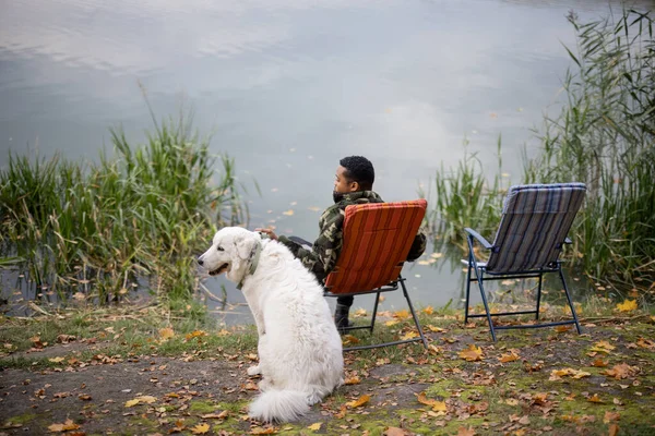 Man vissen in de buurt van hond op rivier of meer kust — Stockfoto