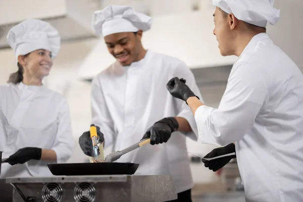 Equipe multirracial de cozinheiros profissionais de uniforme preparando refeições para um restaurante na cozinha — Fotografia de Stock