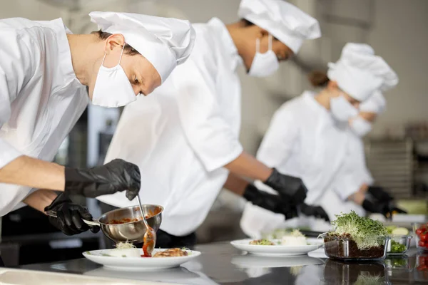 Grupo de cozinheiros terminando os pratos principais enquanto trabalham juntos na cozinha — Fotografia de Stock