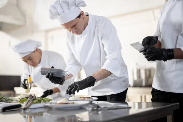 Group of cooks finishing main courses while working together in the kitchen — Stock Photo, Image