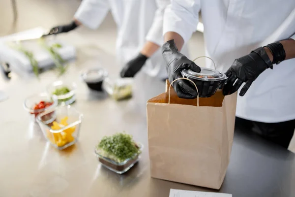 Los cocineros preparan comida para llevar y la envasan en una bolsa de papel para la entrega —  Fotos de Stock