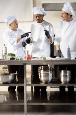 Farklı milletlerden aşçılar restoran menüsü için pişirilmiş yemekleri tadıyorlar.