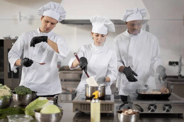 Equipe multirracial de três cozinheiros cozinhar na cozinha profissional — Fotografia de Stock