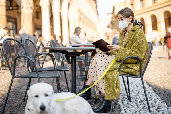 Femme en masque médical assis avec son chien au café extérieur dans la vieille ville italienne — Photo