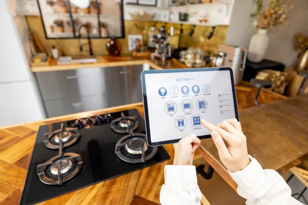 Женщина держит цифровой планшет с запуском интеллектуального домашнего приложения на кухне — стоковое фото