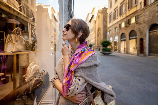 Kadın, eski kasabadaki sokakta çantaları olan bir vitrine bakıyor.