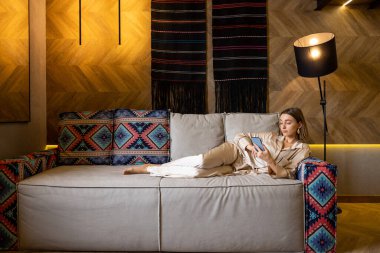 Telefonla oturan bir kadın, modern oturma odasındaki koltukta dinleniyor.