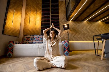 Kadın evde meditasyon yaparken kendini sakin hissediyor.