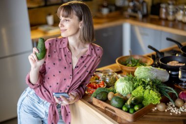Smatphone kullanan bir kadın evde sağlıklı yemek pişiriyor.