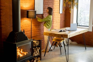 Kadın evdeki tuğla duvara fotoğraf çerçevesi asıyor.