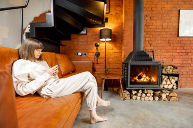 Kanepede rahatça oturan ve evde telefon kullanan bir kadın.