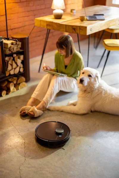 自宅で犬と暖炉に座っている間、ロボット掃除機は床の上で動作します — ストック写真