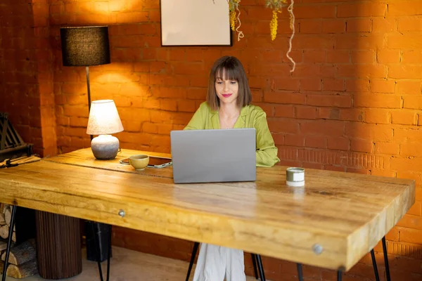 Woman works on laptop while sitting by the wooden table at cozy home — Stock Photo, Image