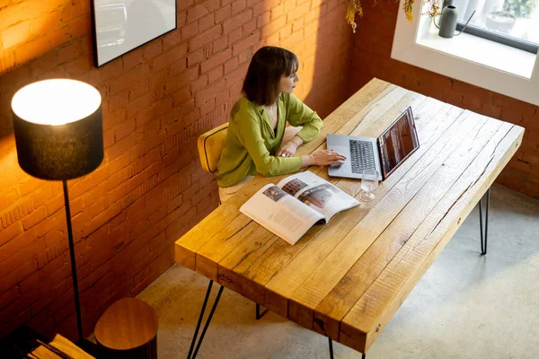 Woman works on laptop while sitting by the wooden table in cozy living room — Stock Photo, Image